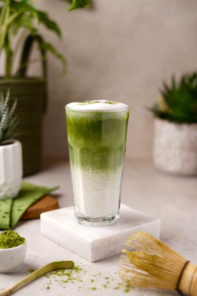 Jeges Matcha latte magas pohárban, mellette Matcha por és bambusz habverő