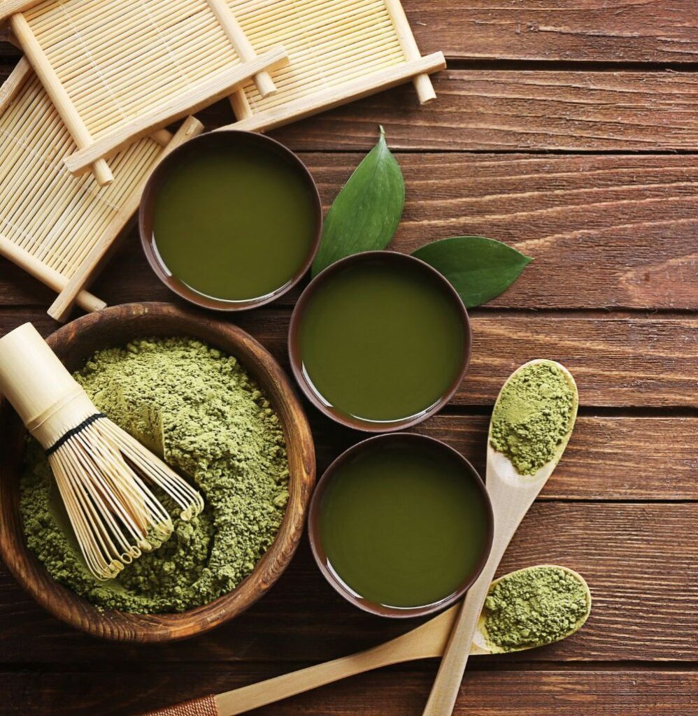 Matcha por, bambusz habverő és frissen elkészített Matcha tea csészékben, faasztalon