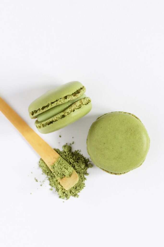 Kész zöld matcha macaronok krémmel megtöltve, fakanálon és szórt matcha porral díszítve, fehér háttér előtt
