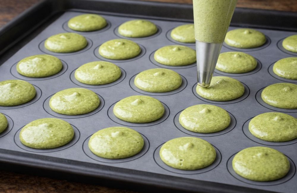 Zöld matcha macaron tészta habzsákból egyenletes körökbe formázva sütőpapíros tepsin, sütés előtt