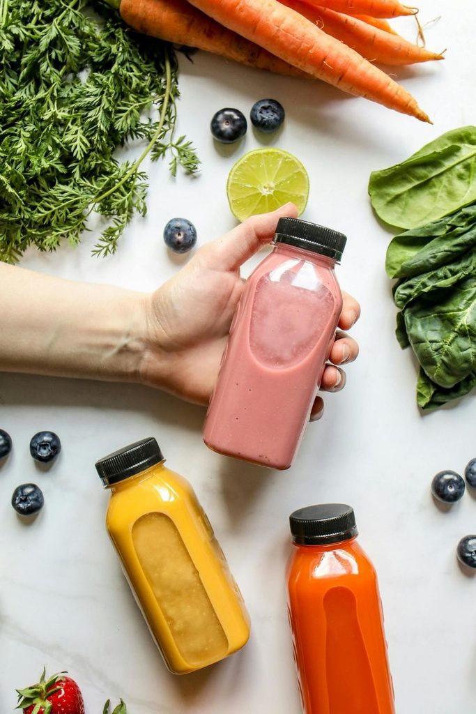 Kézben tartott házi diétás smoothie sárgarépa, spenót és bogyós gyümölcsök között