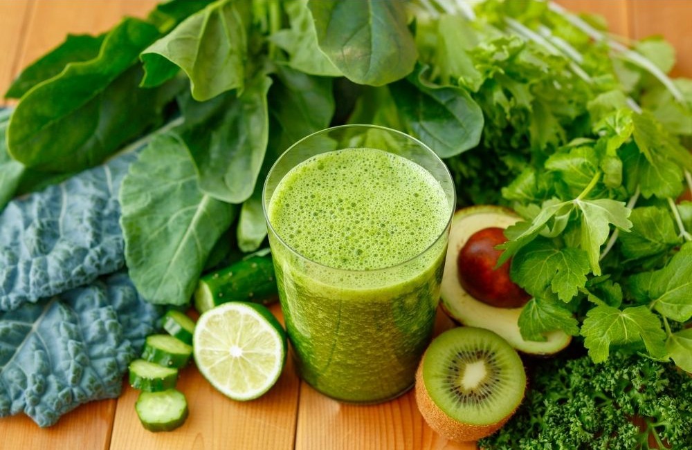 Zöld diétás smoothie pohárban, kelkáposztával, uborkával és kiwivel körülvéve